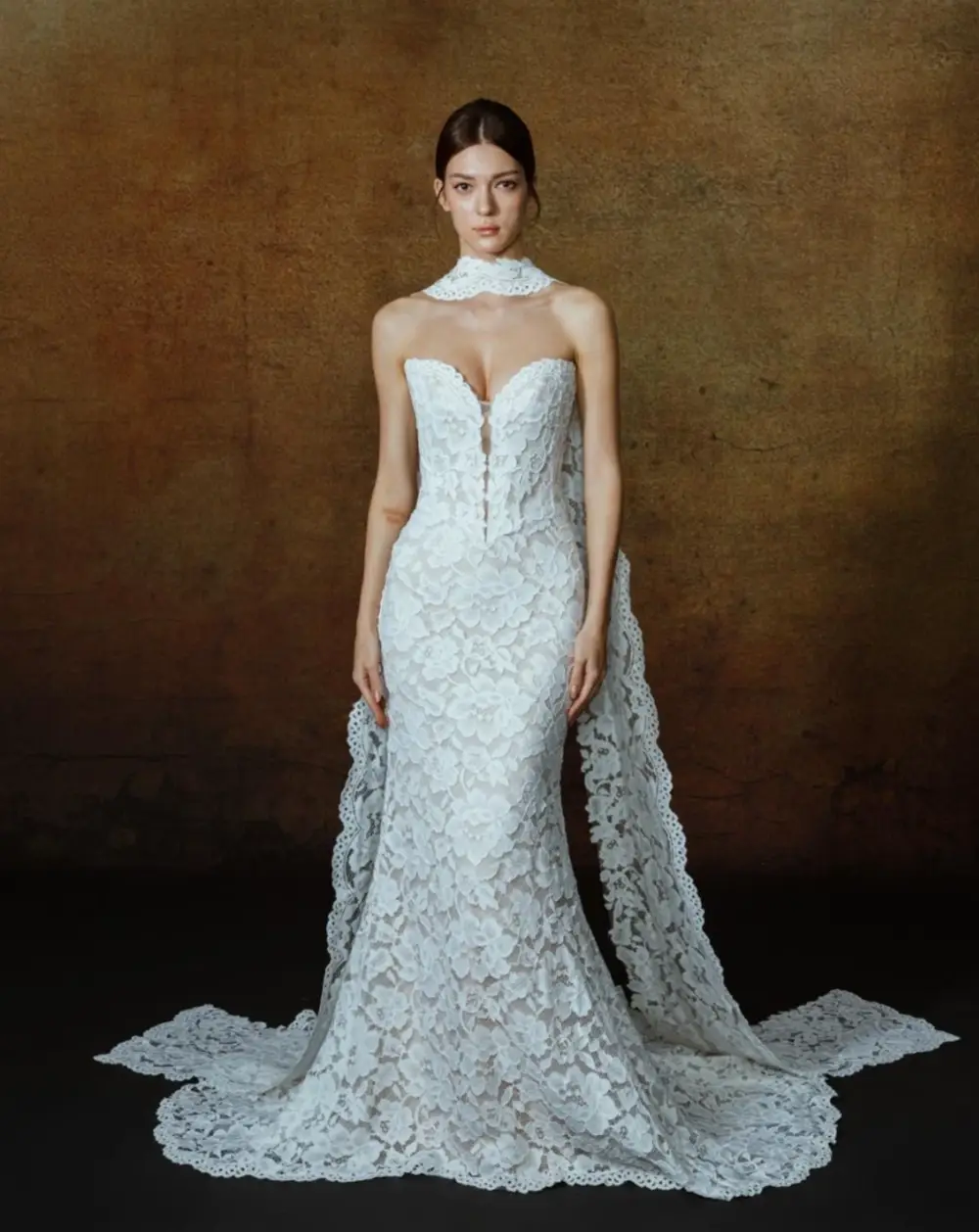 A model wearing an elegant white lace gown with a fitted silhouette and a dramatic train.