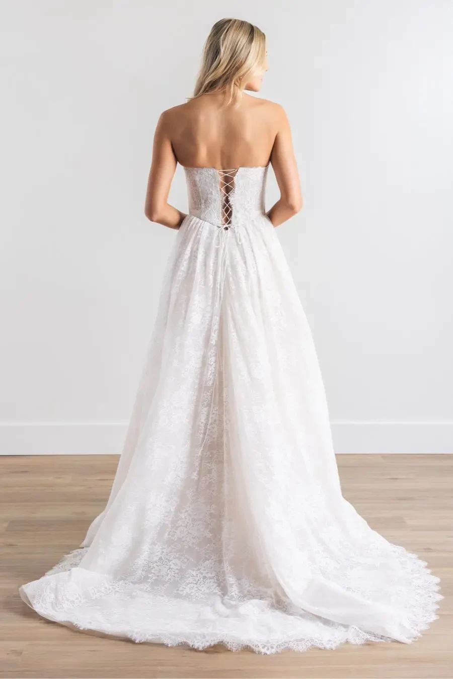 Model is wearing an a-line sleeveless bridal gown that has 3d florals peeking out of the bodice 