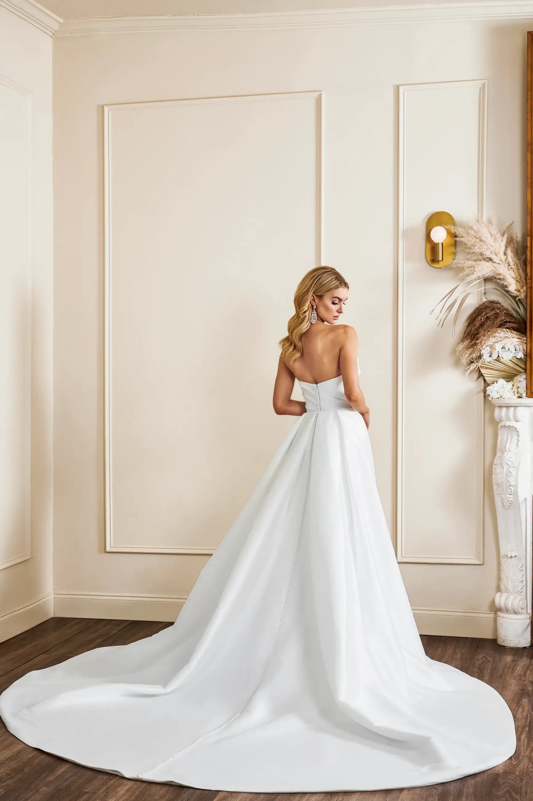 Model is wearing an asymmetric strapless neckline fit and flare bridal gown by kelly faetanini
