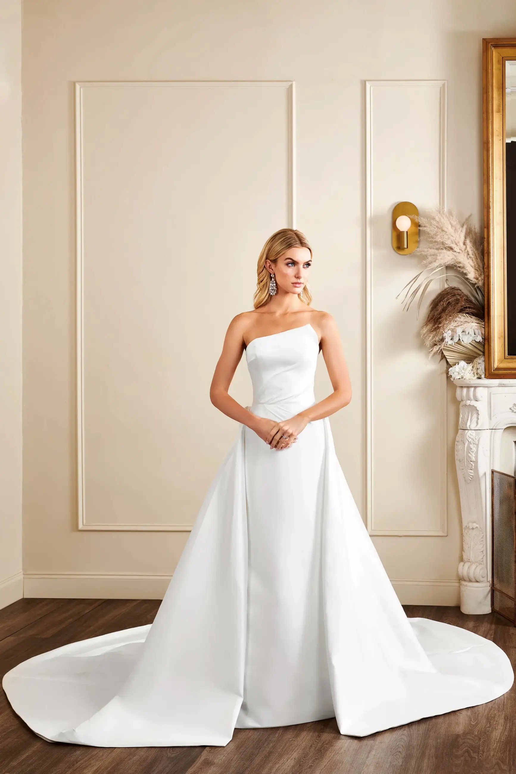 Model is wearing an asymmetric strapless neckline fit and flare bridal gown by kelly faetanini