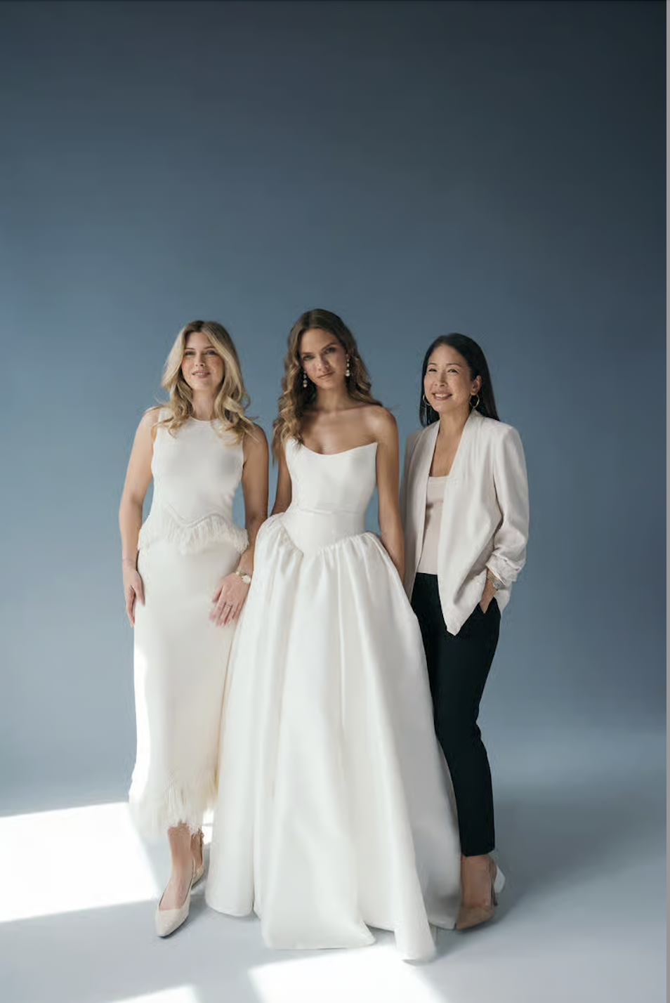 Image shows model in the middle of Hope LaVine and Jenny Yoo, who have collaborated to create a gown called Danielle, which model is wearing (the dress is a lightweight ball gown wedding dress with a strapless neckline and structured bodice)