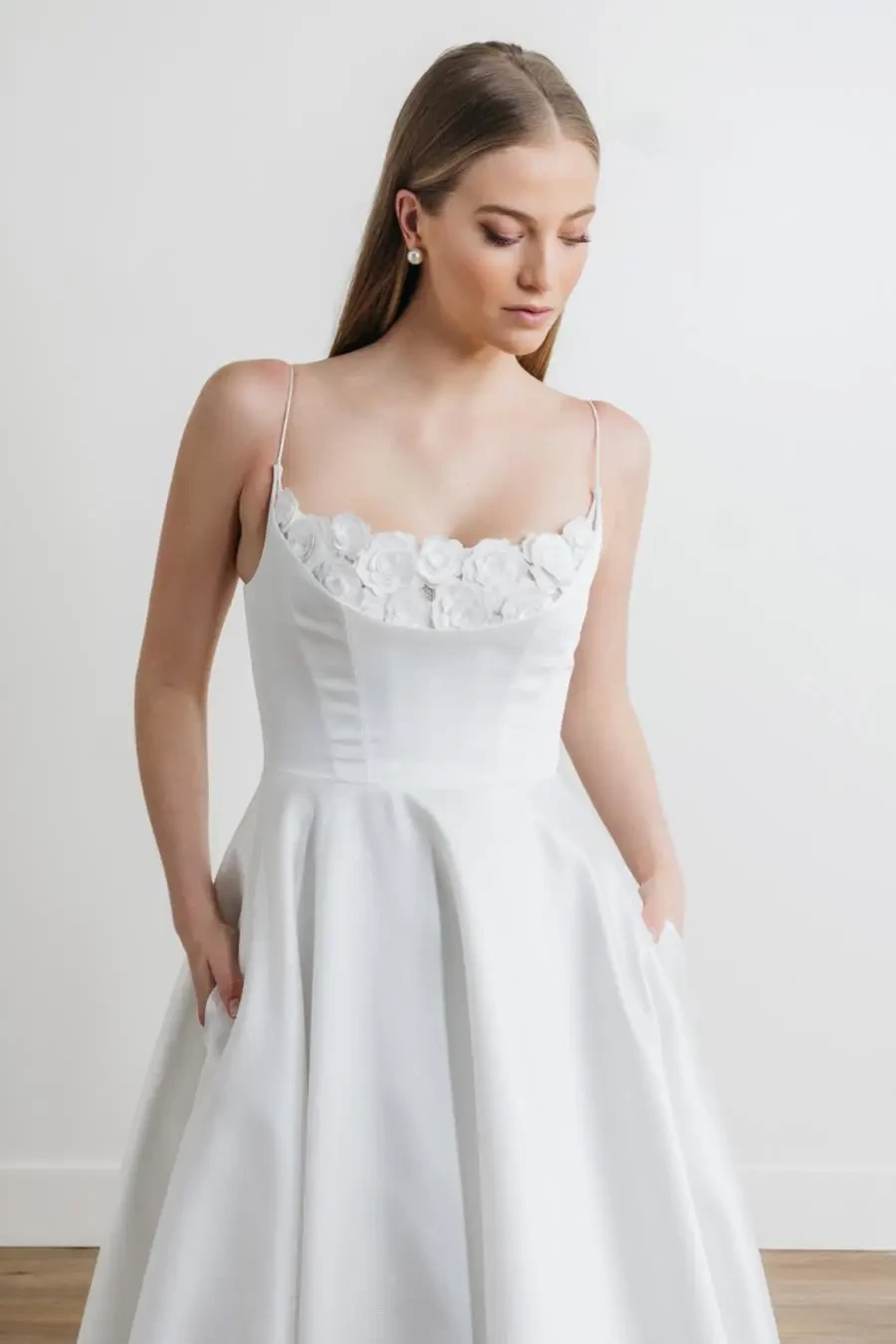 model is wearing a sleeveless a-line bridal gown with a minimalist skirt and 3d florals peeking out of the bodice
