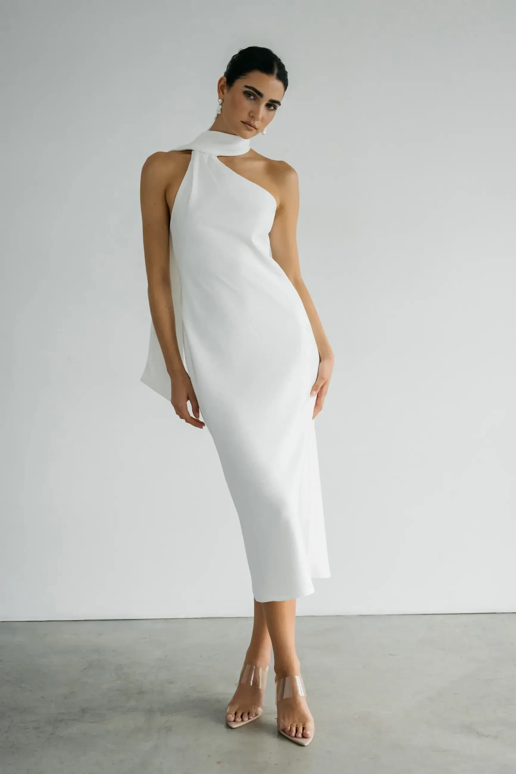 A model wearing a chic white dress poses against a plain background.